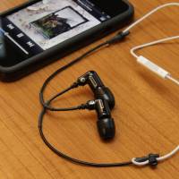 a pair of black earphones.Next to a black touch phone.That has a black protective case.